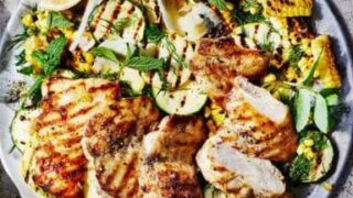 A plate of grilled chicken breasts served with charred corn, zucchini slices, fresh herbs, and lemon wedges on a light surface—perfect for easy One Pot Summer Dinners that capture the season’s freshest flavors.