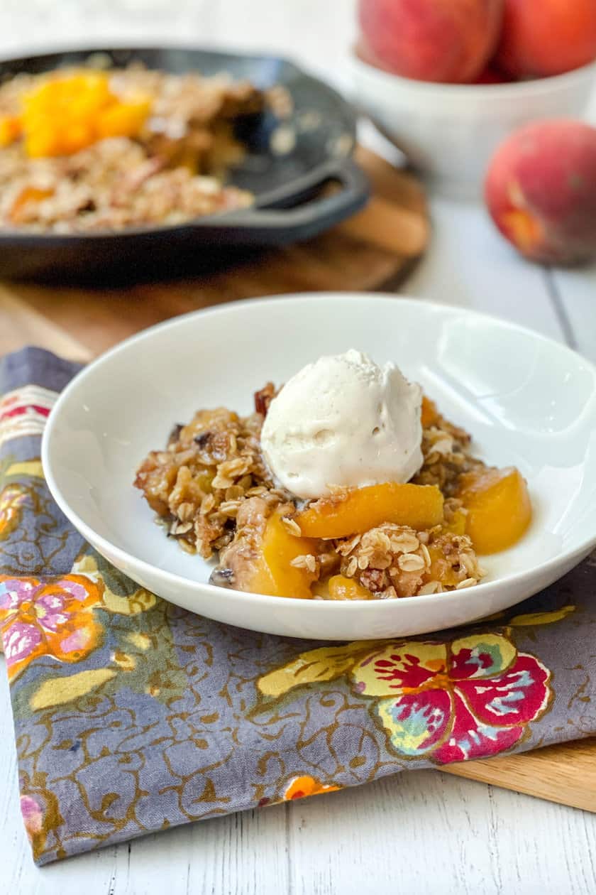 Side view of Peach Crisp in a white bowl with vanilla ice cream