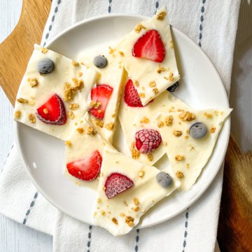 Frozen yogurt bark pieces topped with strawberries, blueberries, raspberries, and granola on a white plate.