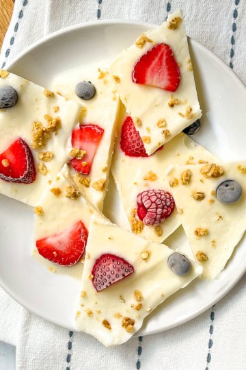 Frozen yogurt bark pieces topped with strawberries, blueberries, raspberries, and granola on a white plate.