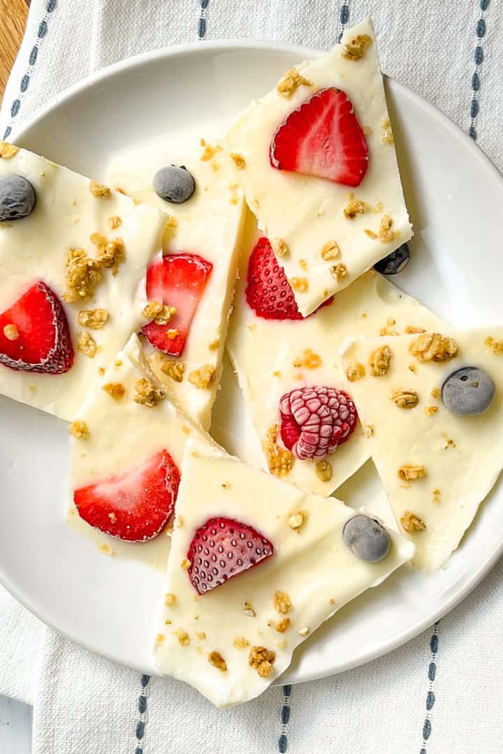 Frozen yogurt bark pieces topped with strawberries, blueberries, raspberries, and granola on a white plate.