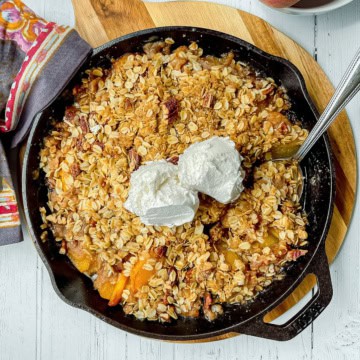 Peach crisp in a cast iron skillet with two scoops of vanilla ice cream on top.