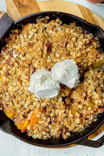 Peach crisp in a cast iron skillet with two scoops of vanilla ice cream on top.