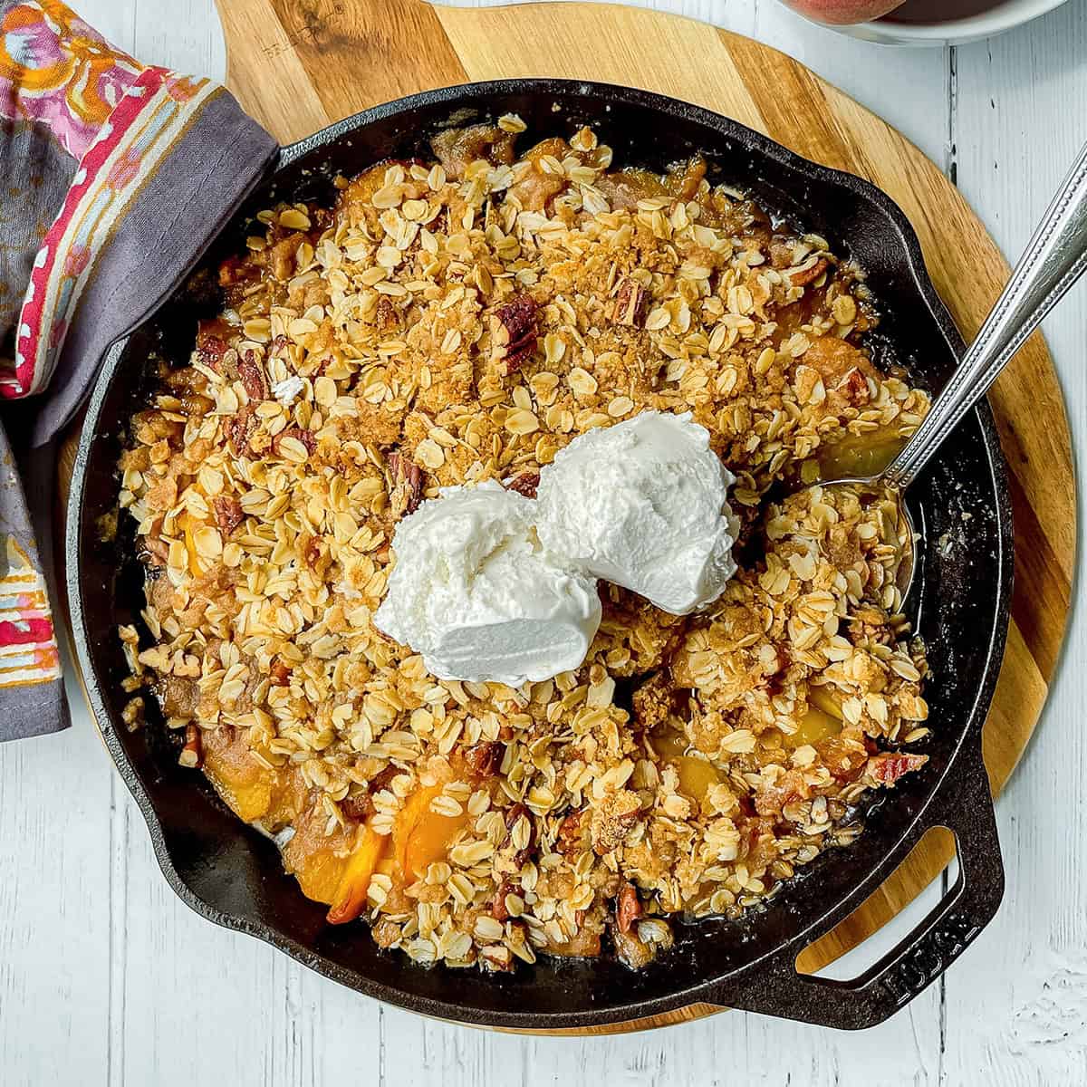 Peach crisp in a cast iron skillet with two scoops of vanilla ice cream on top.