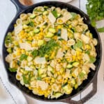 Orecchiette zucchini pasta in a skillet with corn, spinach, cheese shavings, and fresh herbs.