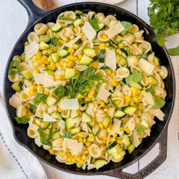 Orecchiette zucchini pasta in a skillet with corn, spinach, cheese shavings, and fresh herbs.