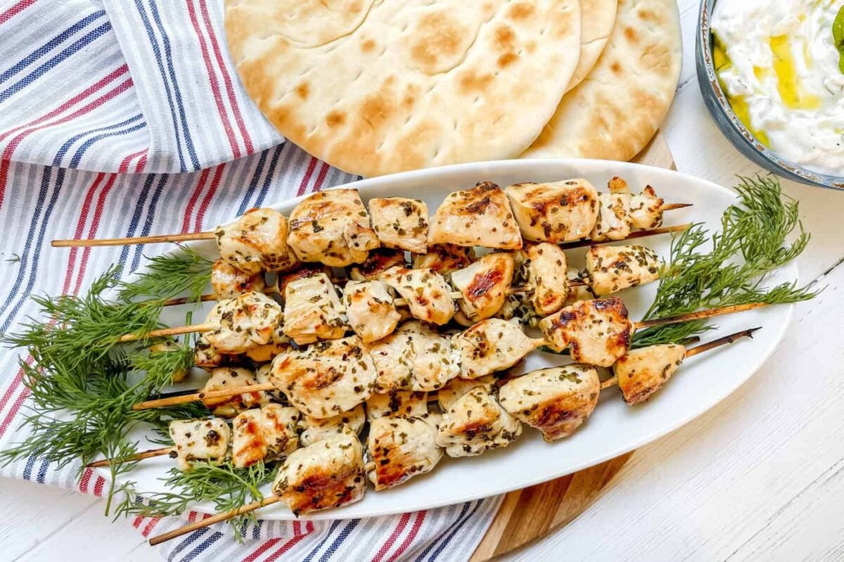 Top view chicken souvlaki skewers on a white platter with pita bread