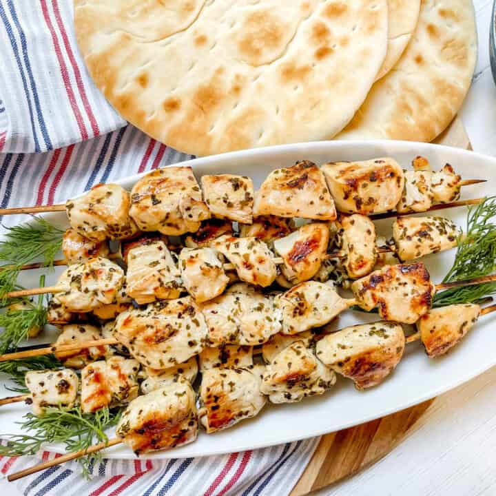 Top view chicken souvlaki skewers on a white platter with pita bread