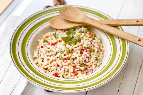 Side view of Macaroni Salad in a green and white bowl with serving spoons
