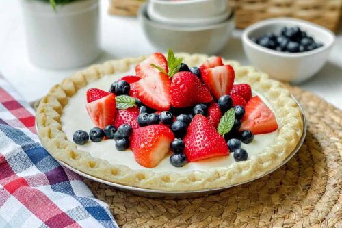 Side view of Berry Vanilla Pudding Pie with a strawberries and blueberries