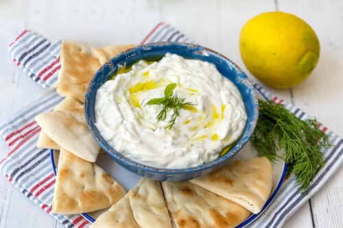 Side view of Tzatsizi Sauce in a blue bowl with wedges of pita