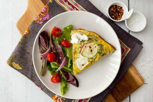 Top view of a slice of Mediterranean Zucchini Frittata with fresh greens