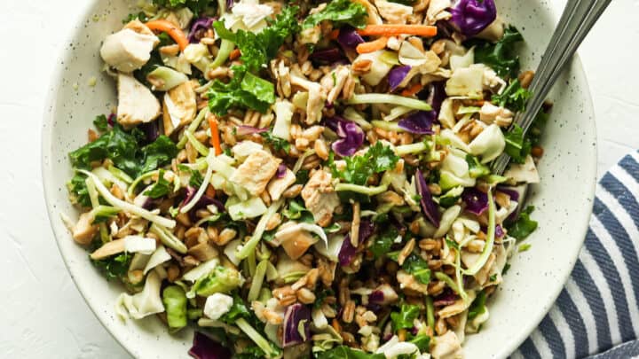 A bowl of chopped salad with greens, cabbage, chicken pieces, seeds, and vegetables—perfect for healthy 20 minute dinners. A fork rests by the side, with a striped cloth beside the bowl.