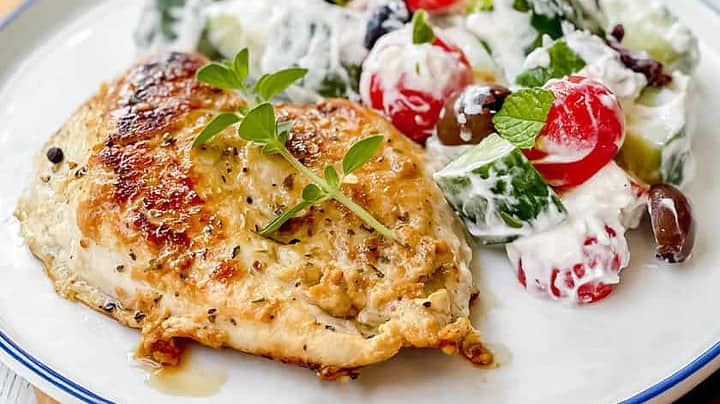 Closeup view of Greek Chicken with Cucumber Salad on a blue and white plate