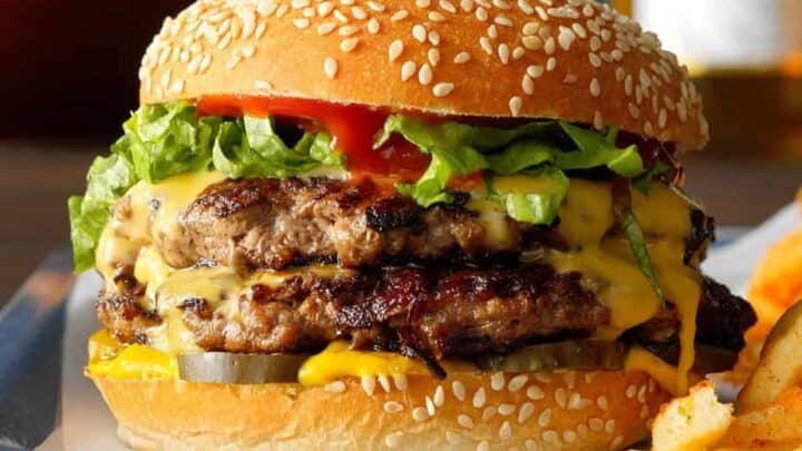 Side view of hamburger with double patties on a sesame bun with lettuce, mustard, and melting cheese.