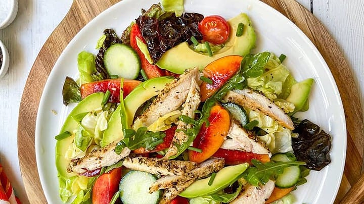Top view of Stone Fruit Chicken Salad on a Round Wood Cutting Board with Nectarines