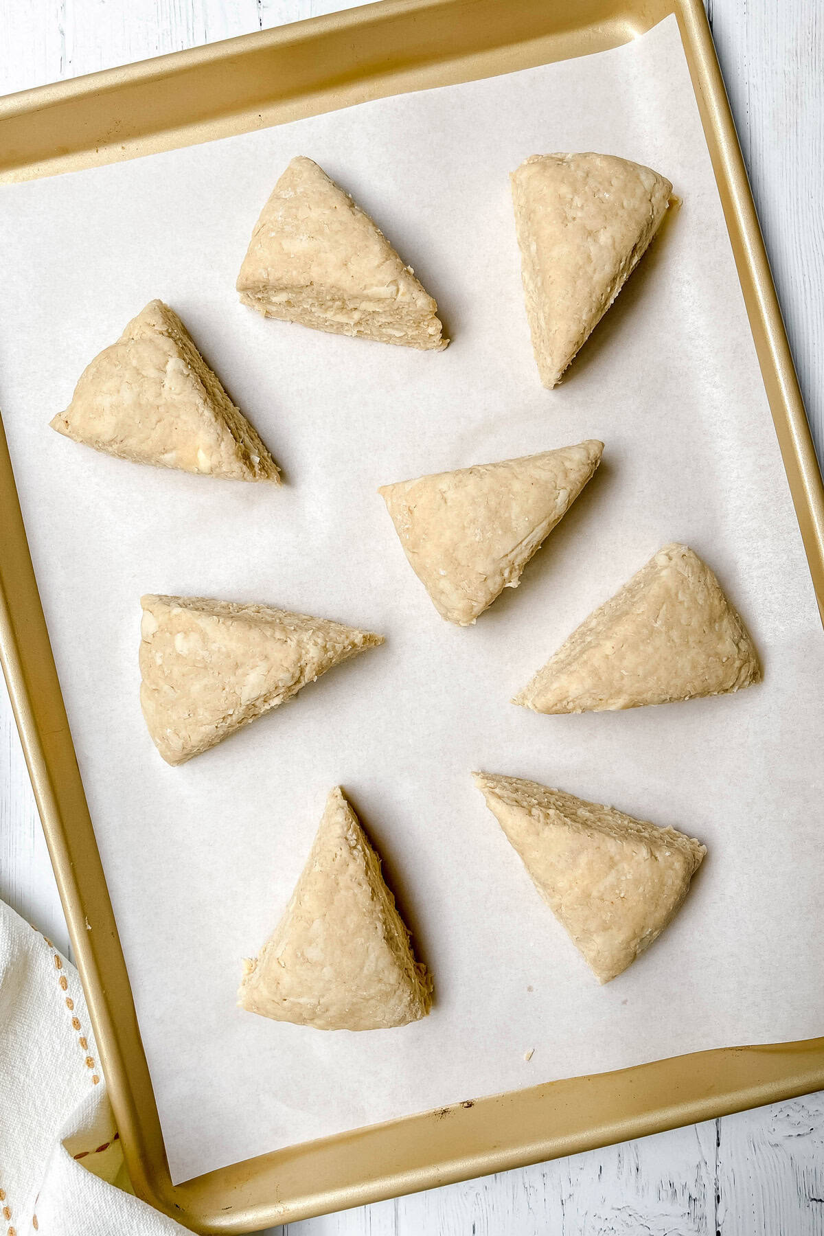 Unbaked apple scones on a parchment lined baking sheet brushed with cream and ready for the oven.