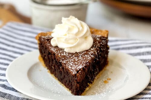 Front view of sliced Brownie Pie topped with powdered sugar and whipped cream