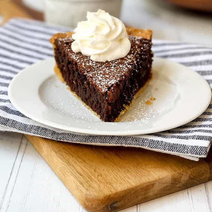 Front view of sliced Brownie Pie topped with powdered sugar and whipped cream