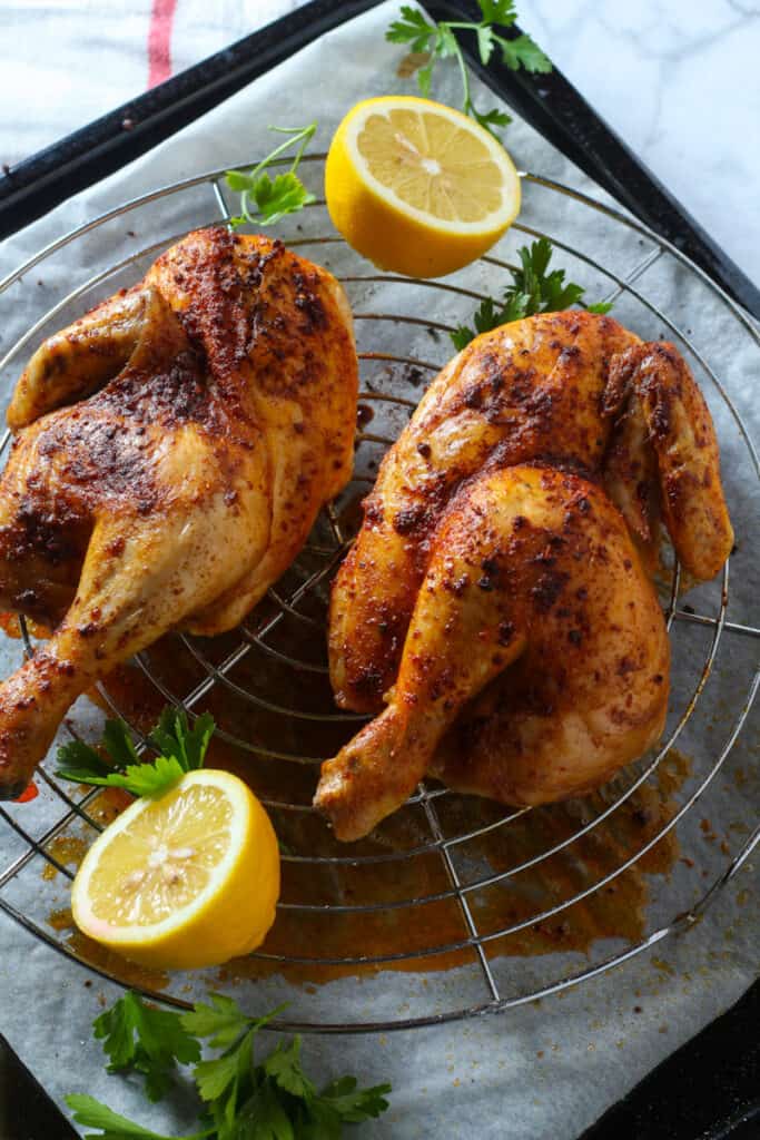 Two roasted spatchcock chickens on a wire rack with parchment paper, garnished with lemon halves and parsley-perfect for your Oktoberfest recipes.