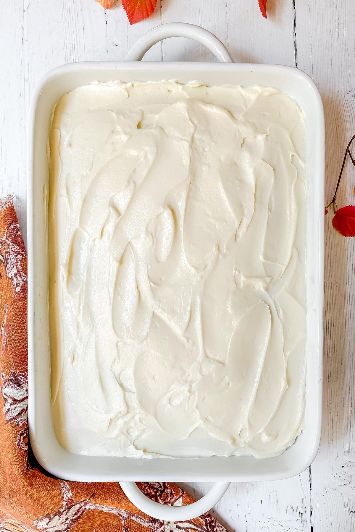 Adding cream cheese frosting to baked pumpkin bars in a 9 x 13 inch baking pan.