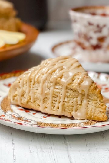 An glazed apple cinnamon scones sits on a Spode small tea plate with a teacup in the background.