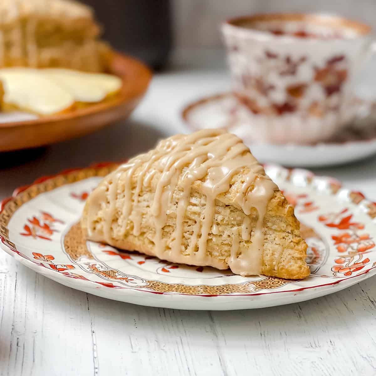 An glazed apple cinnamon scones sits on a Spode small tea plate with a teacup in the background.