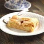 Closeup view of sliced apple strudel on a white plate with tea.