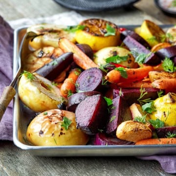 Roasted fall vegetables on a silver baking sheet with a fork and garnish with fresh parsley.
