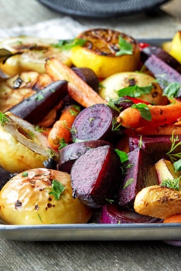 Roasted fall vegetables on a silver baking sheet with a fork and garnish with fresh parsley.