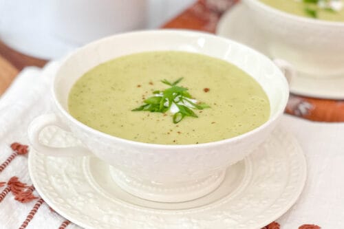 Side view of Zucchini Potato Cheddar soup in a white bowl with green onions and nutmeg