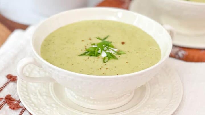 Side view of Zucchini Potato Cheddar soup in a white bowl with green onions and nutmeg