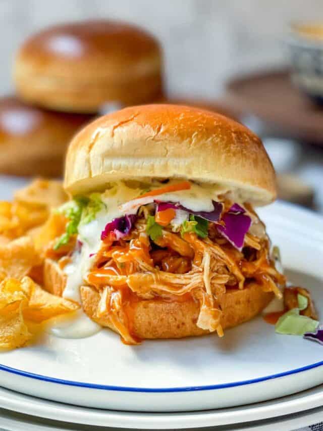 Front view of tender slow cooker Buffalo chicken and coleslaw on a bun with chips