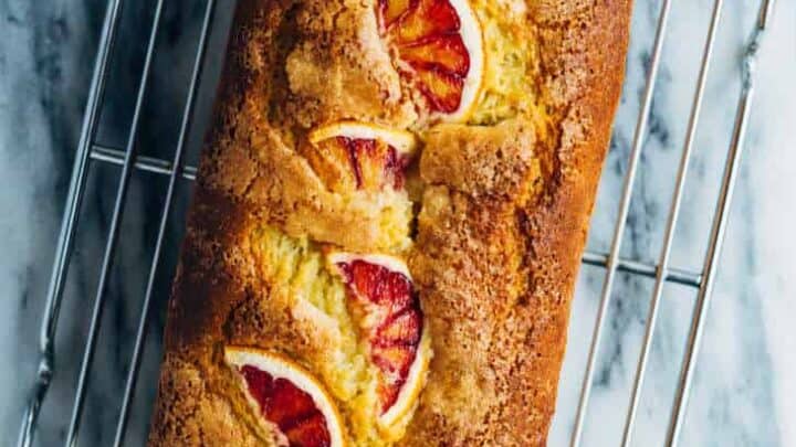 A loaf of bread with three slices of blood orange on top, perfect for Fall Mediterranean Diet Dinners, rests on a metal cooling rack over a marble surface.