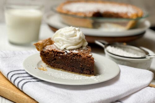 Side view of sliced Brownie Pie with whipped cream on a white plate