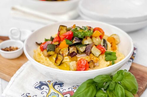 Side view of Sheet Pan Ratatouille over creamy polenta in a white bowl