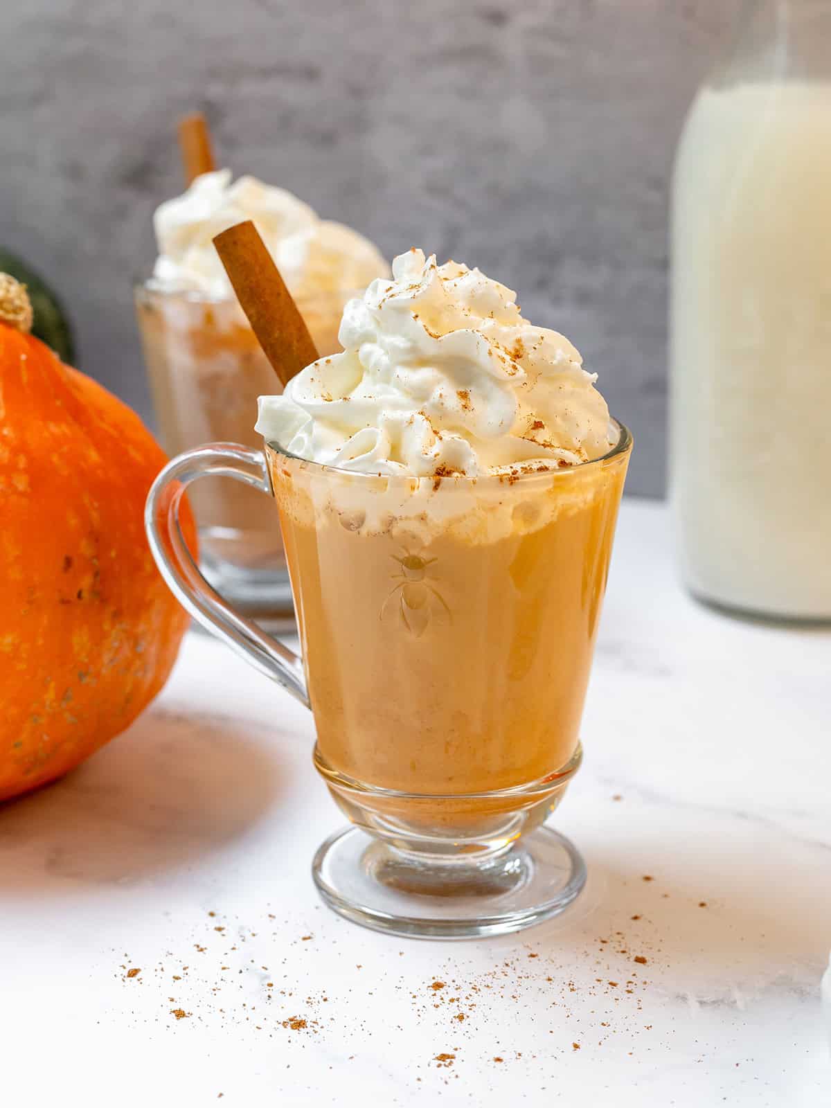 Pumpkin spice latte in a glass mug topped with whipped cream, cinnamon, and a cinnamon stick.