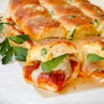 Close-up of Hawaiian Roll Sliders: pull-apart bread sliders filled with melted cheese, tomato sauce, and basil, topped with a golden, herbed crust and garnished with parsley.