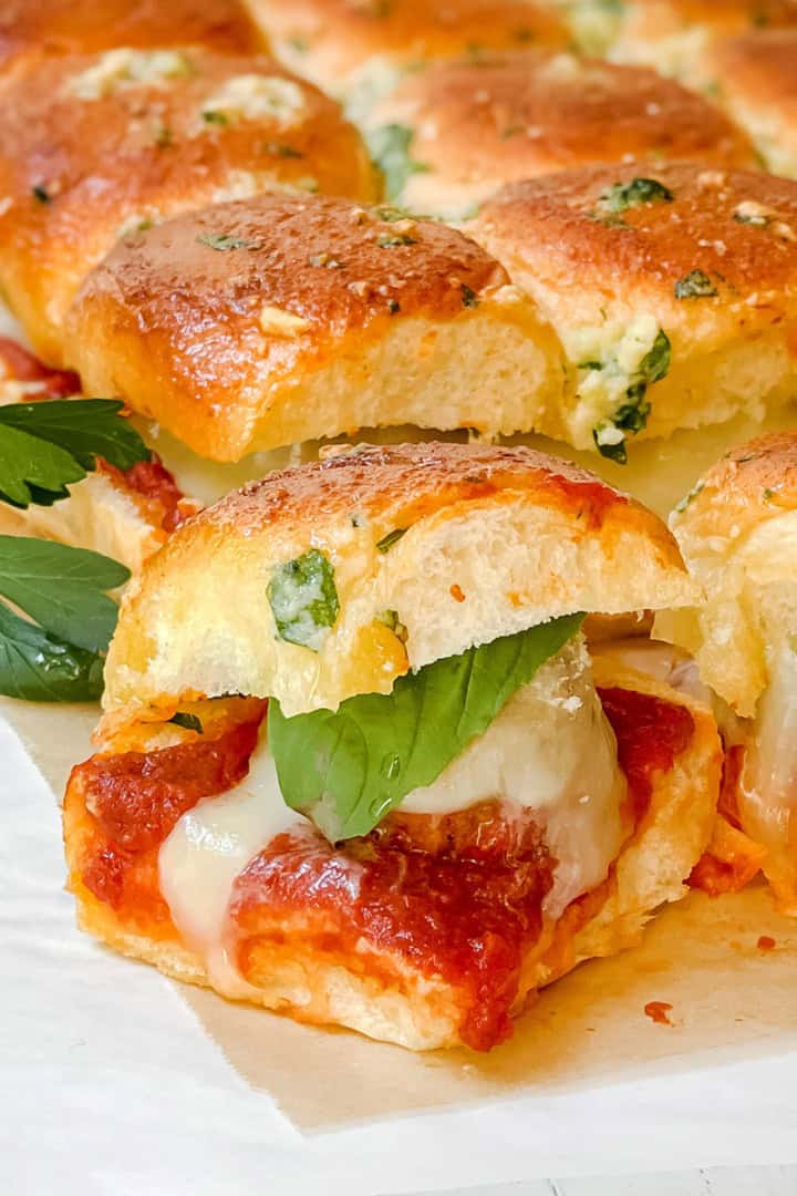 Close-up of Hawaiian Roll Sliders: pull-apart bread sliders filled with melted cheese, tomato sauce, and basil, topped with a golden, herbed crust and garnished with parsley.