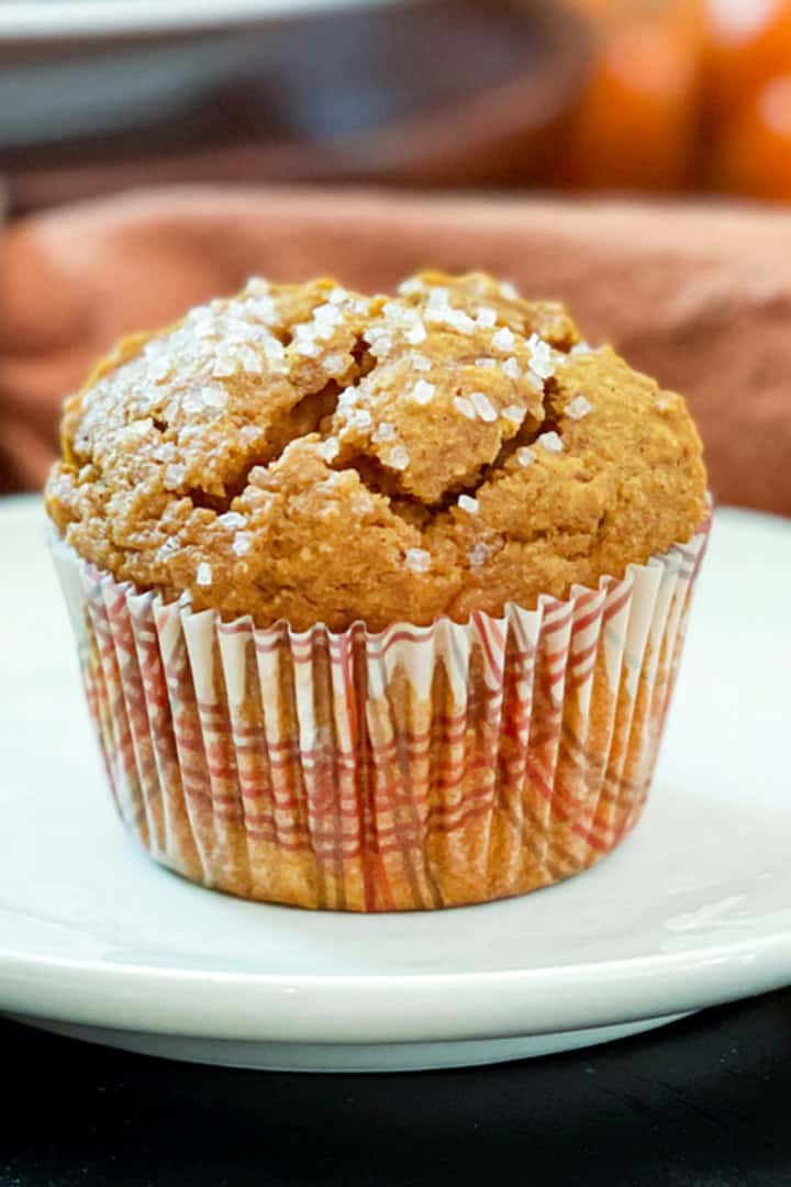 Square image of healthy pumpkin muffin in a fall paper sleeve resting on a small plate.