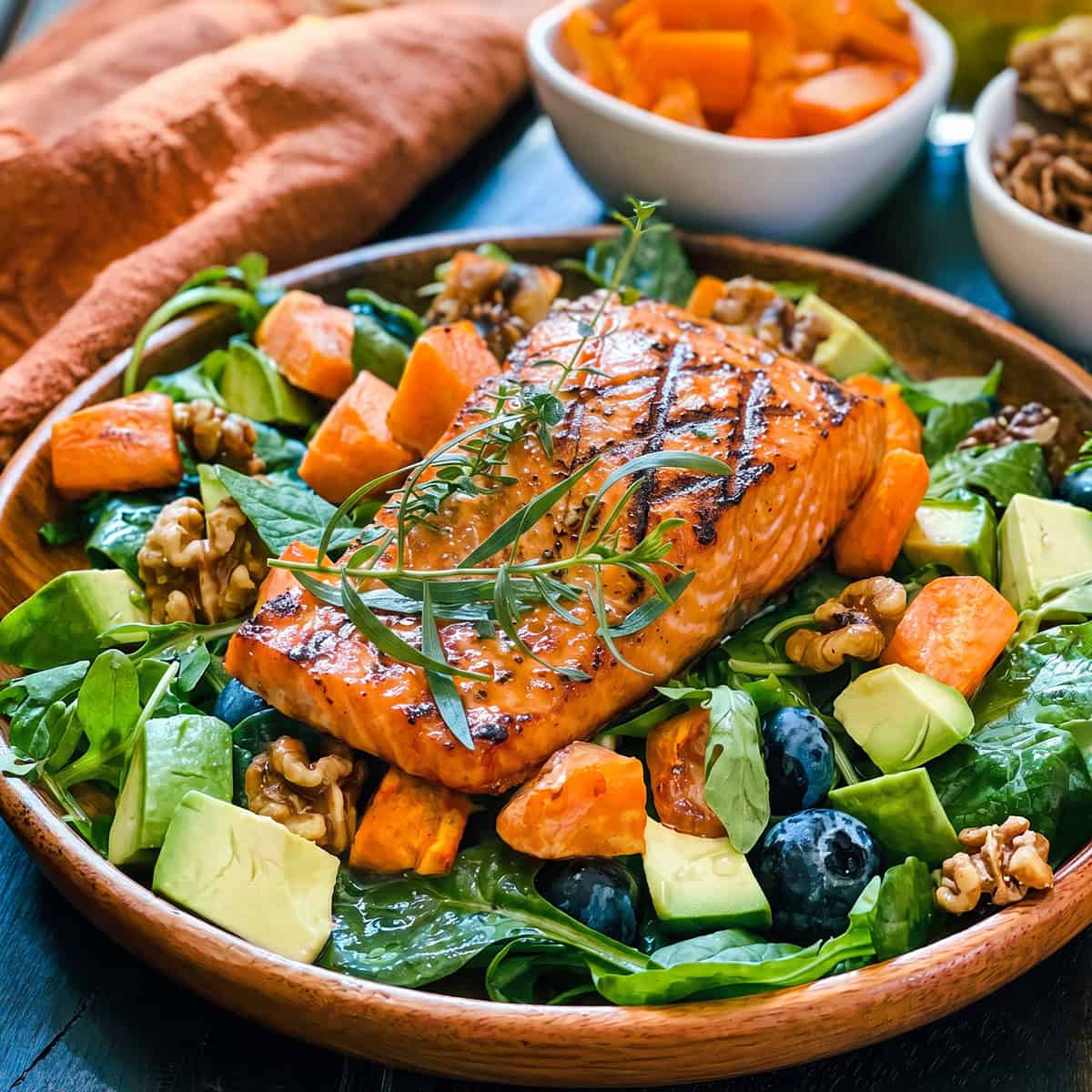 Grilled Salmon fillet on a bed of harvesst greens including roasted butternut squash, avocado and fresh blueberries.