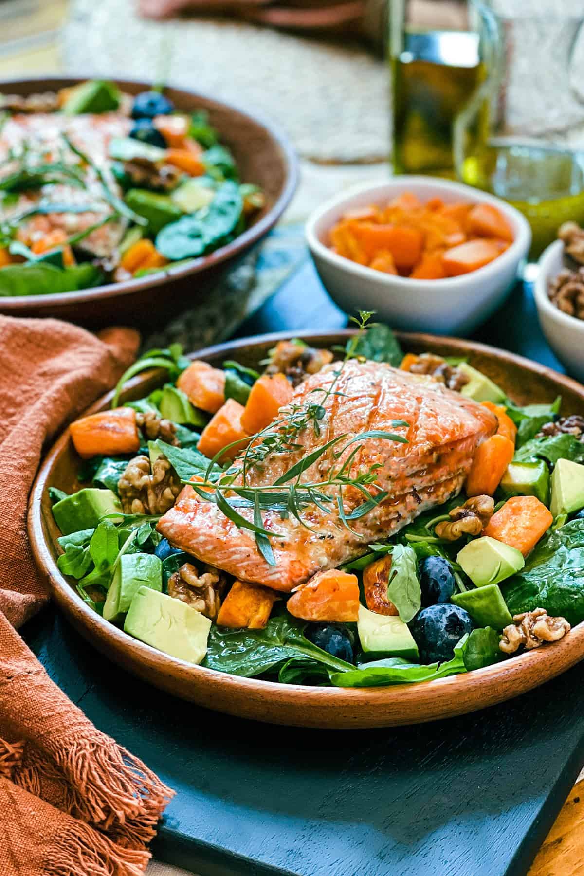 Grilled salmon fillet on a bed of greens including roasted butternut, toasted walnuts, avocado, spinach and blueberries resting in a wooden plate.