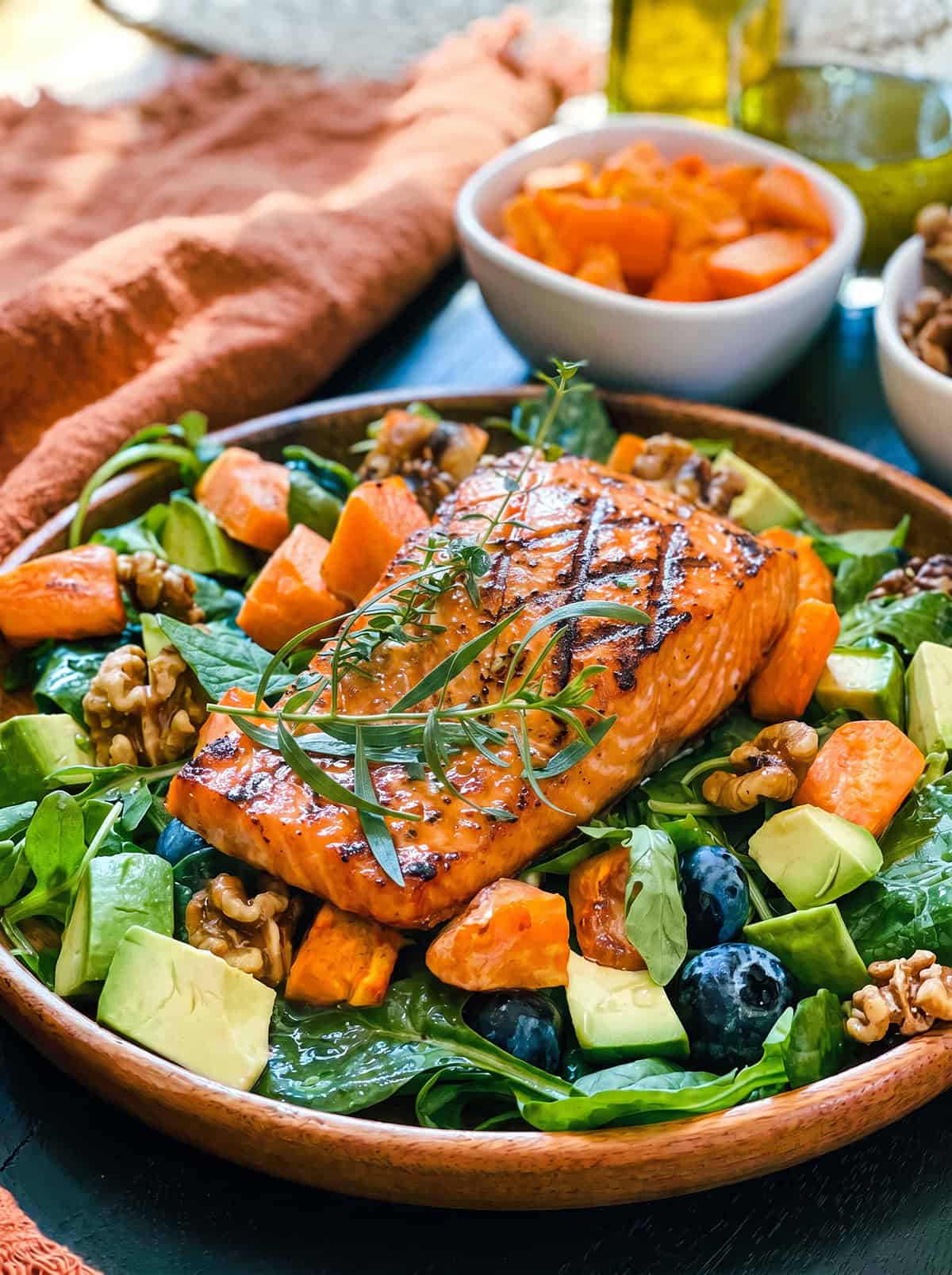 Grilled salmon fillet on a bed of greens including roasted butternut, toasted walnuts, avocado, spinach and blueberries resting in a wooden plate.