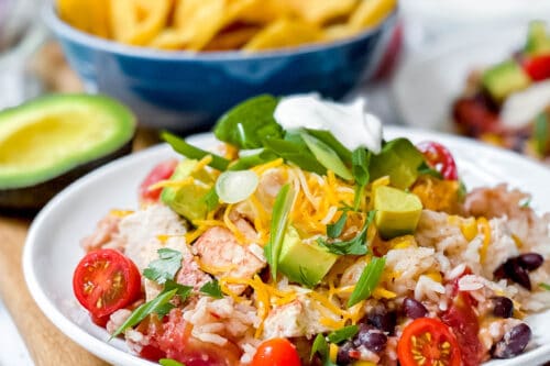 Side view of crockpot chicken and rice burrito in a white bowl with green onions, avocado and sour cream