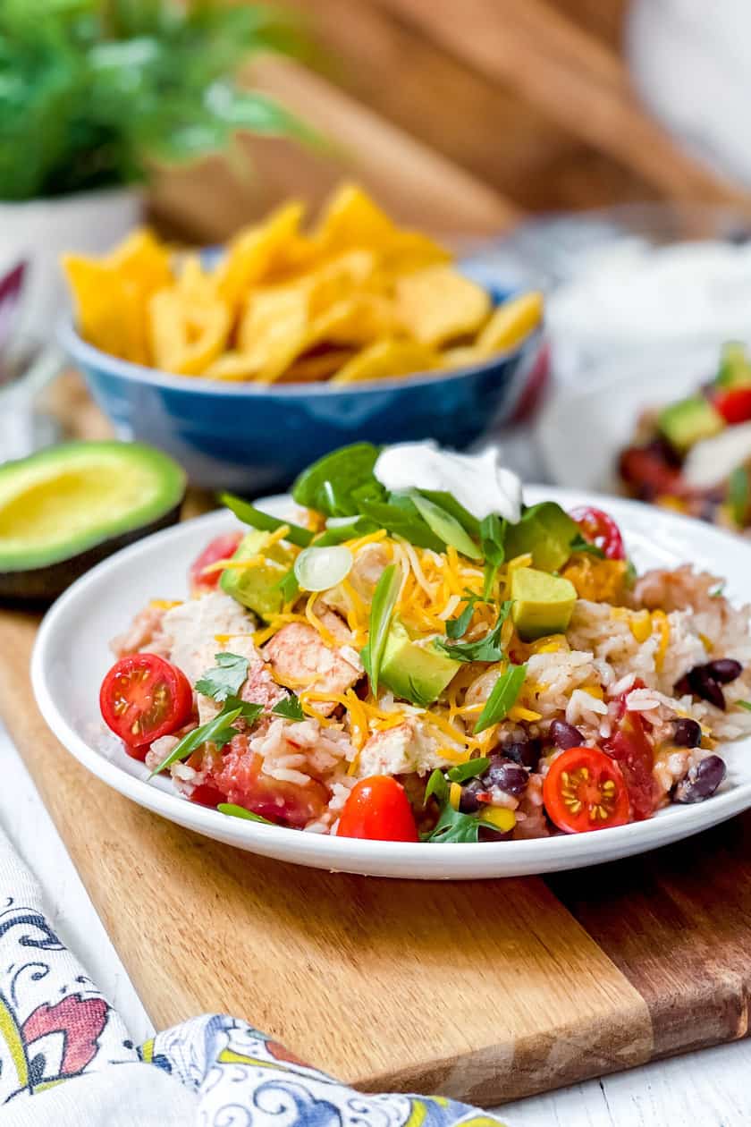 Side view of crockpot chicken and rice burrito in a white bowl with green onions, avocado and sour cream