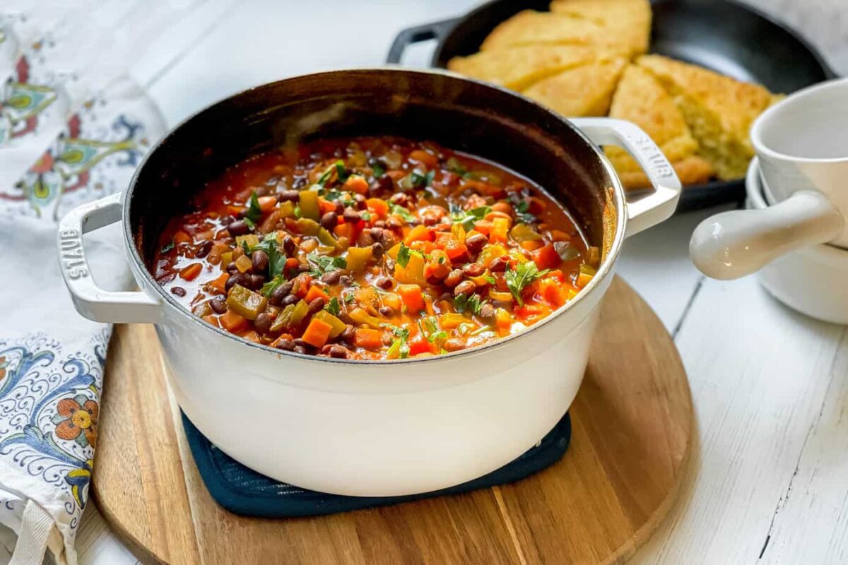 Side view of Vegetarian Chili in a white Dutch oven with cornbread in the background