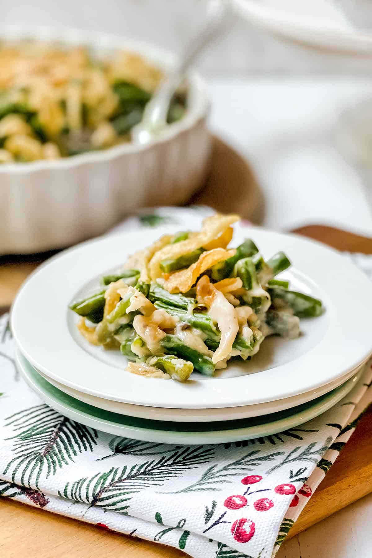 Serving of baked green bean casserole on a white plate with more in the background.