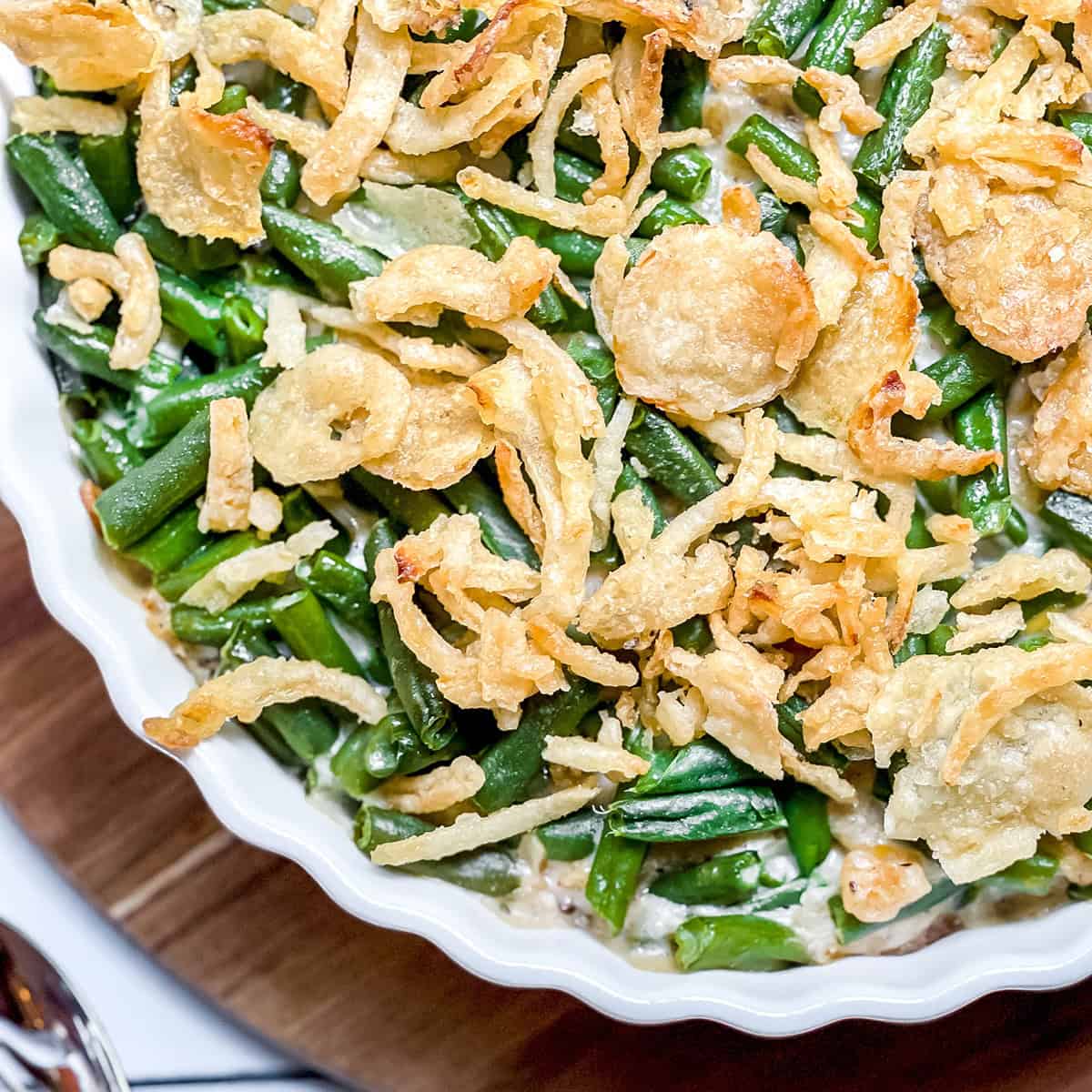 Green bean casserole in a white flutted baking dish, topped with crispy onions, ready for baking.