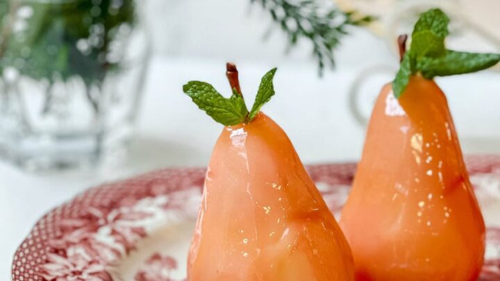 Side closeup view of poached pears on a red and white platter with fresh mint leaves