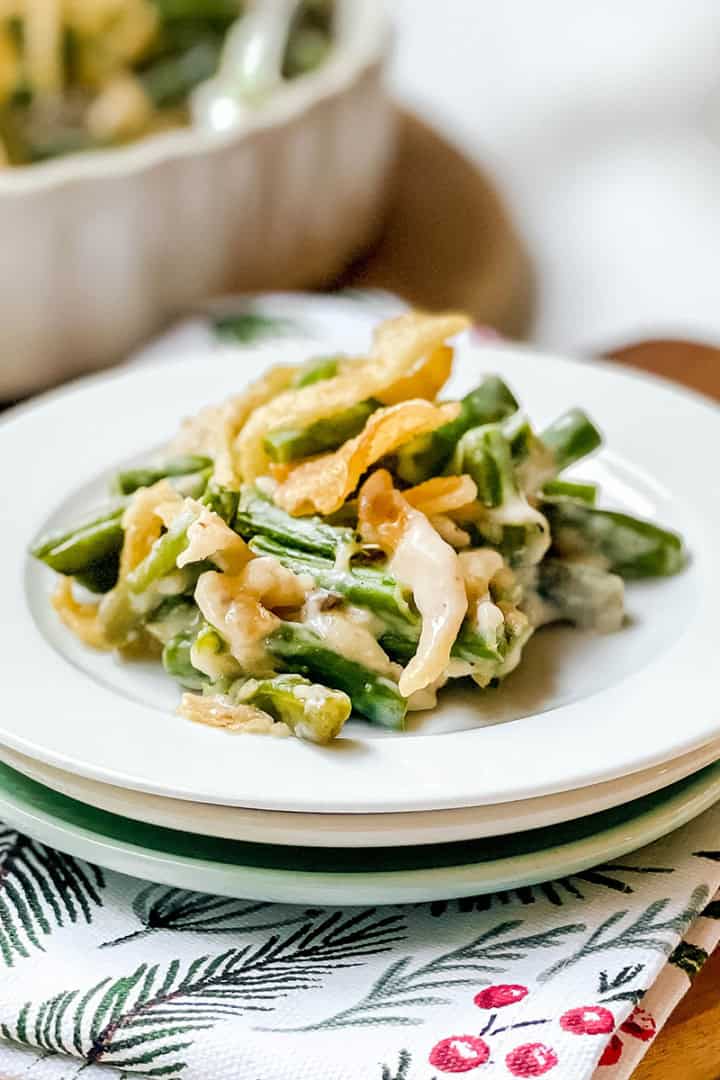 Square image of a serving of green bean casserole on a plate sitting on a festive linen.